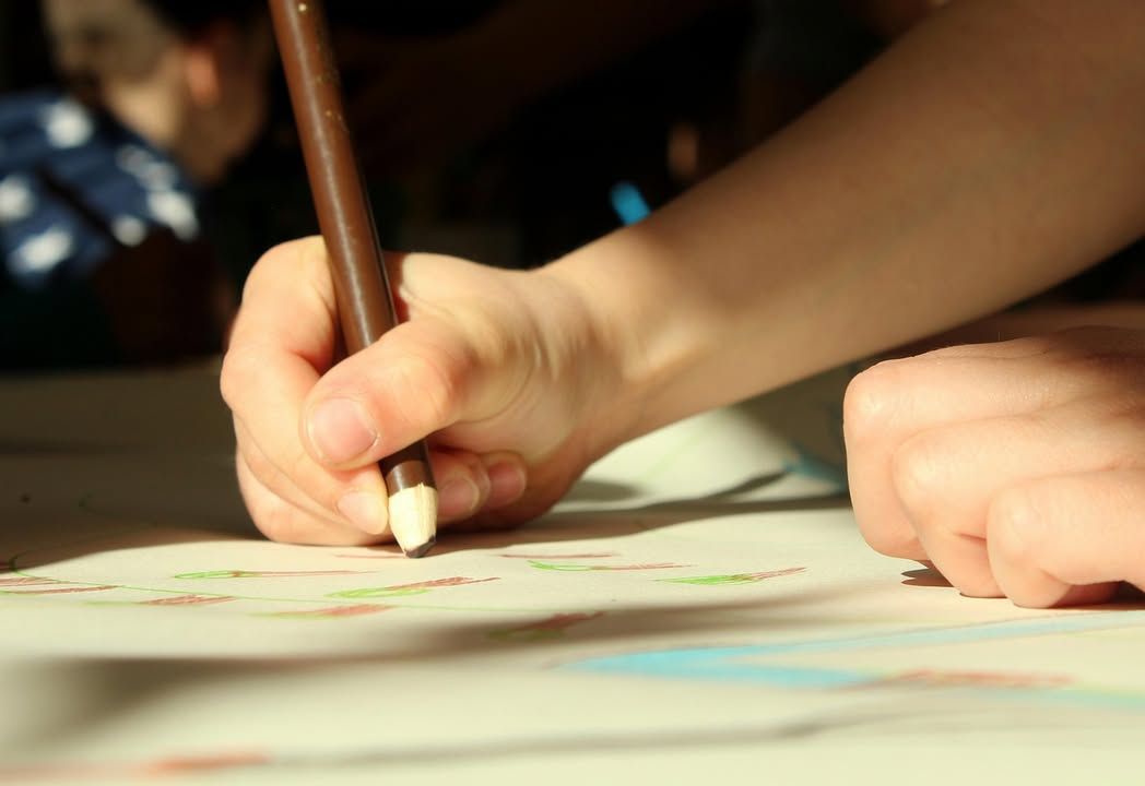 Mano de un niño dibujando en una hoja con crayones de colores.