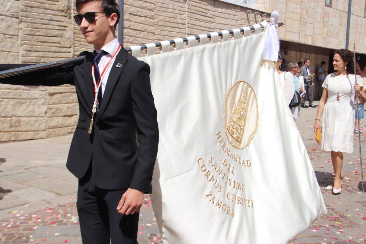 Joven con traje negro portando bandera del Corpus Christi en Zamora