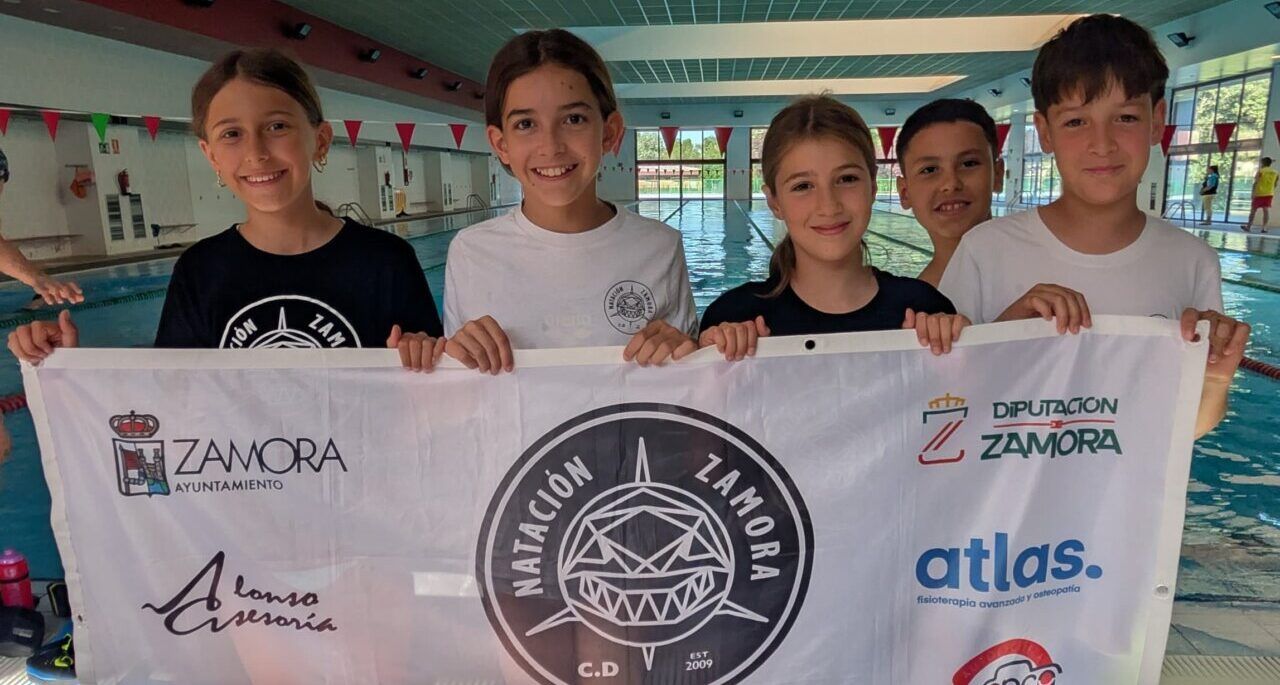 Niños sosteniendo una bandera del Club Deportivo Natación Zamora en una piscina.