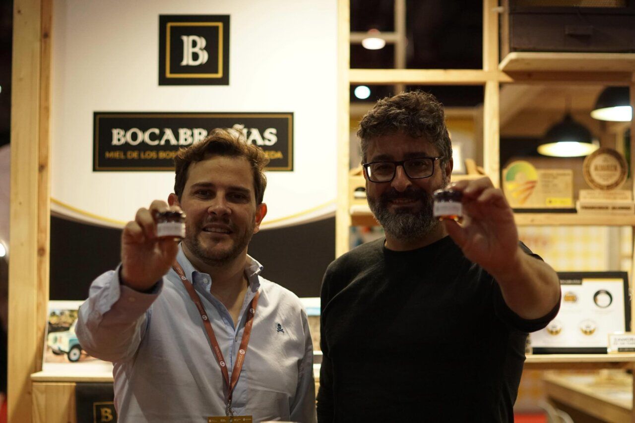Dos hombres sosteniendo tarros de miel en un stand de feria