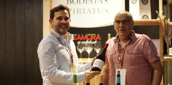 Dos hombres sosteniendo una botella de vino en un stand de Bodegas Viriatus