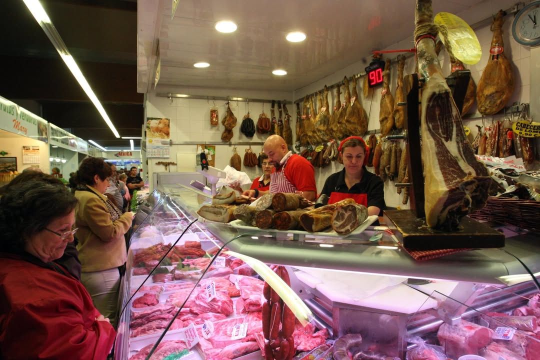 Mercado municipal con productos cárnicos y clientes comprando