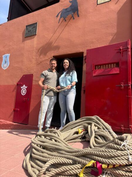 Una joven y un hombre sosteniendo una maroma frente a un edificio rojo