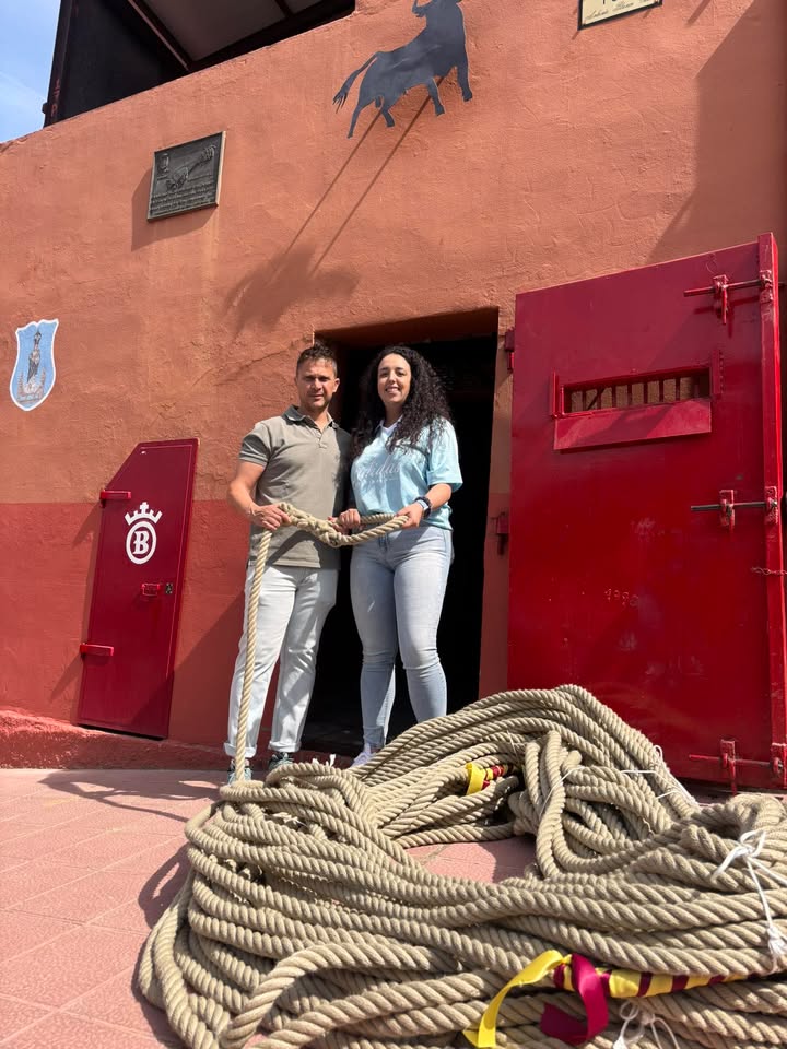 Una joven y un hombre sosteniendo una maroma frente a un edificio rojo