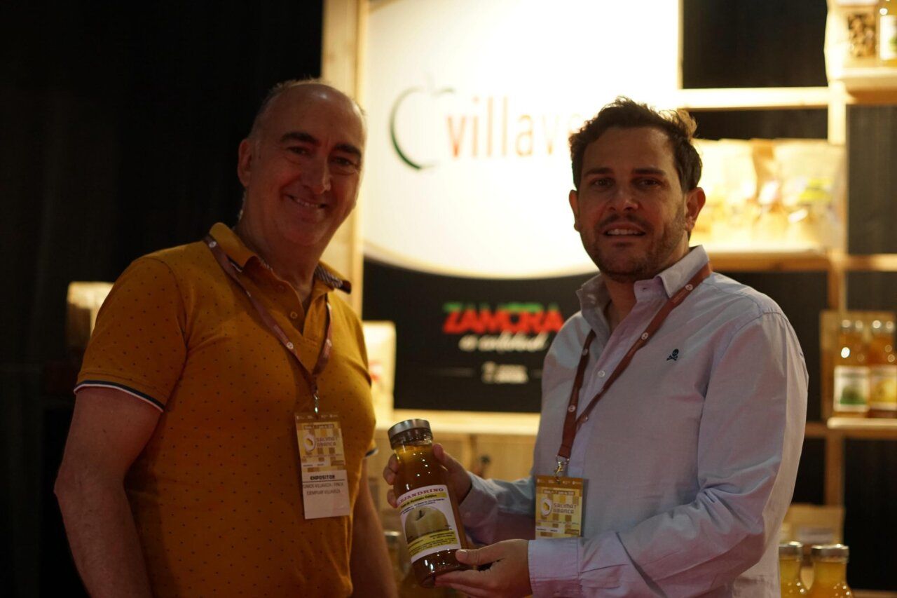 Dos hombres sosteniendo un frasco en un stand de la feria