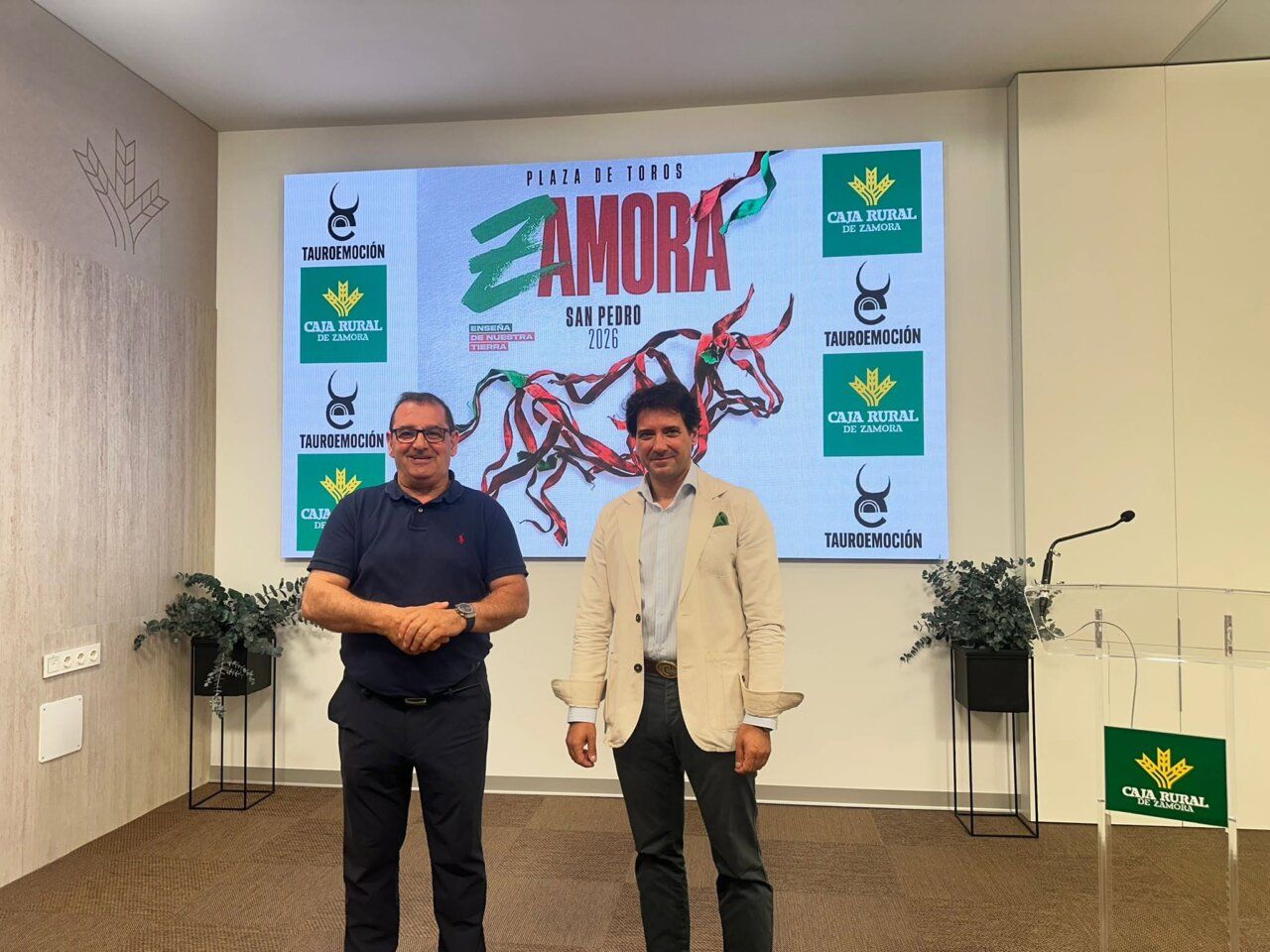 Dos hombres posando frente a una pantalla con el logo de San Pedro 2026