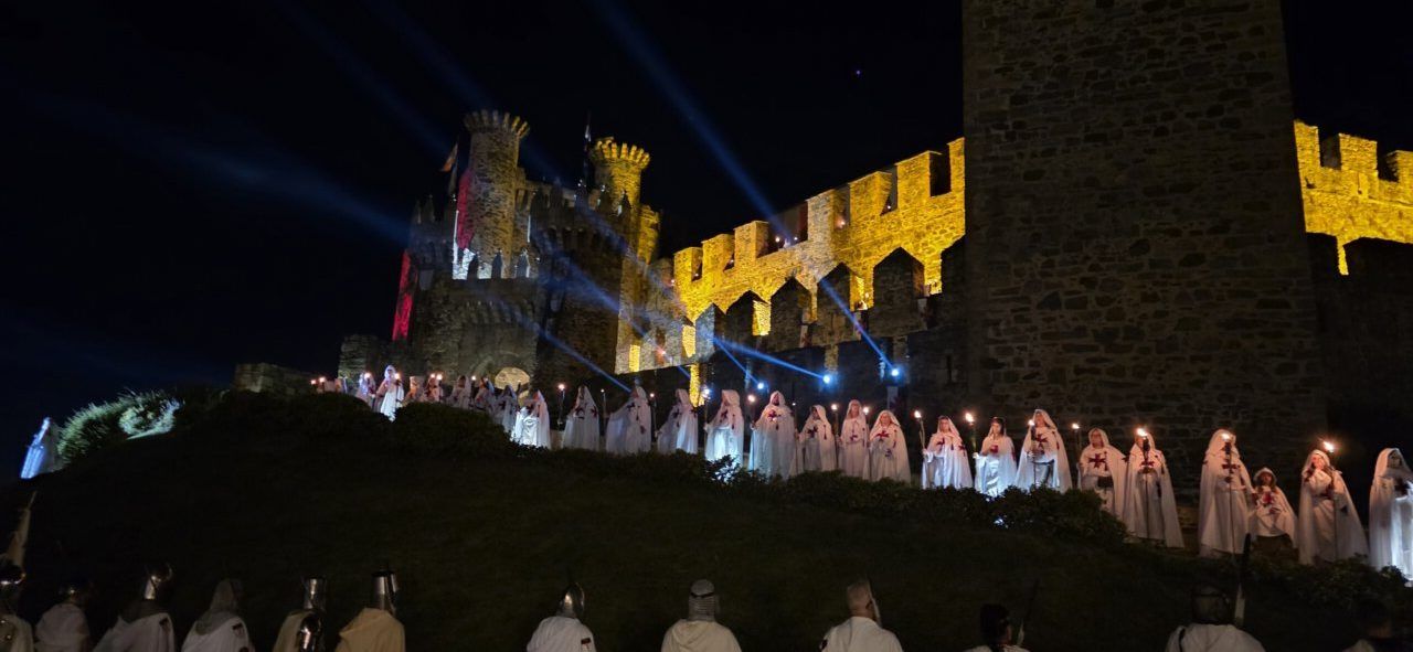 Desfile templario en Ponferrada con participantes vestidos de blanco y castillo iluminado
