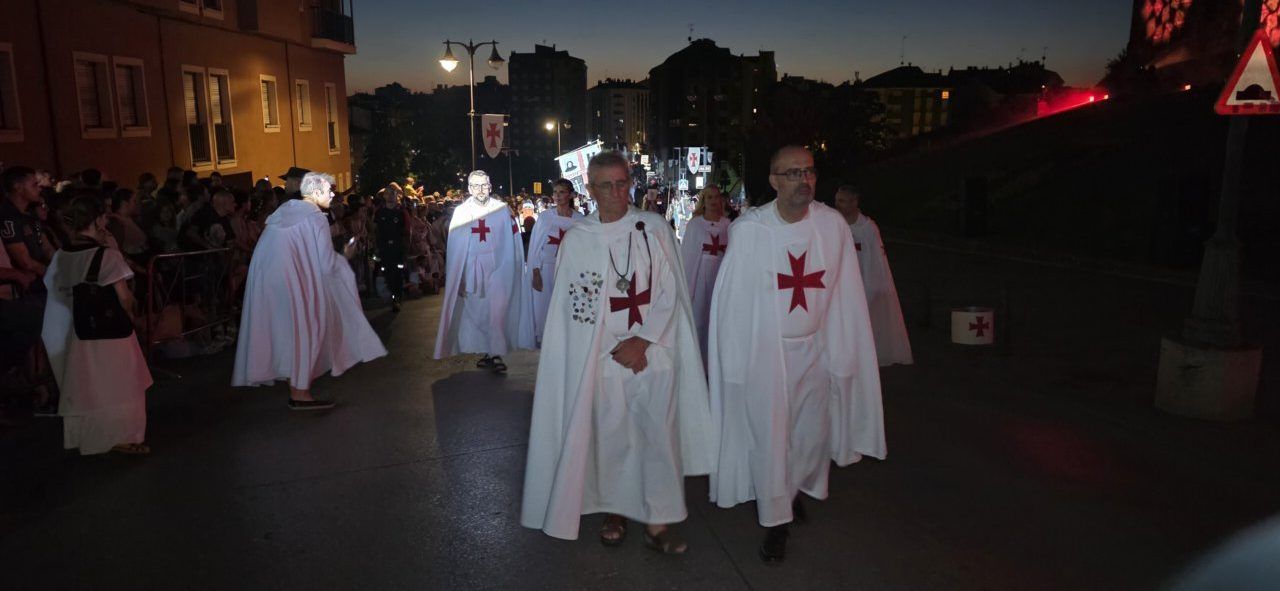 Grupo de personas con capas blancas y cruces rojas en un desfile nocturno.