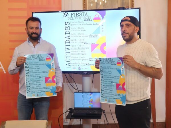 Dos hombres sosteniendo carteles de actividades para el Día del Comercio en Pinilla.