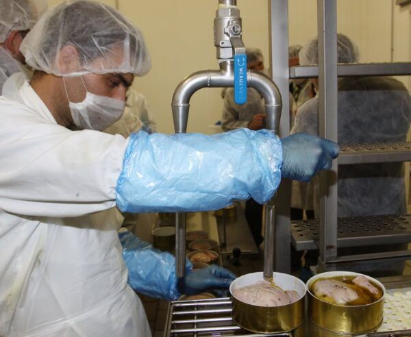 Trabajador en planta de producción manipulando alimentos enlatados