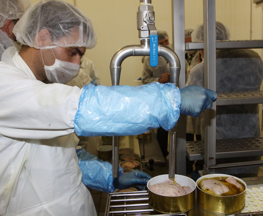 Trabajador en planta de producción manipulando alimentos enlatados