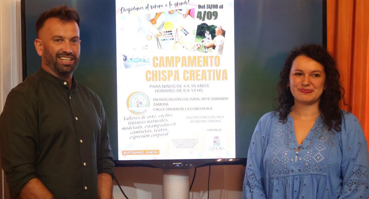 Dos personas posando frente a un cartel del campamento Chispa Creativa en Zamora.