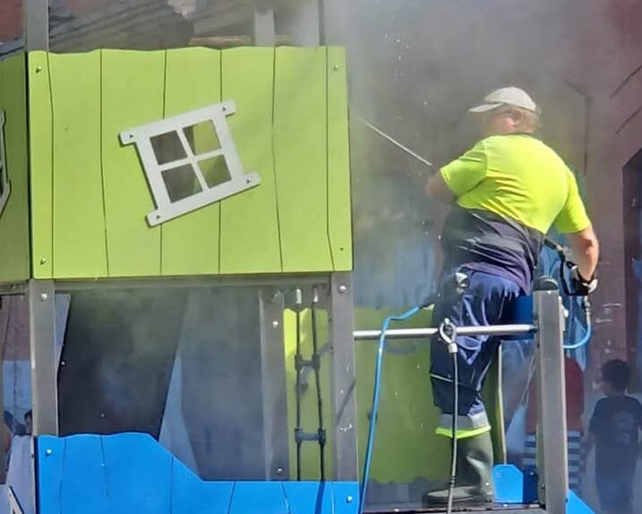 Operario limpiando un parque infantil en Mota Vieja con una manguera