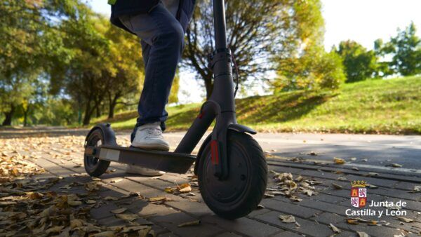Persona montando un patinete eléctrico en un camino rodeado de hojas