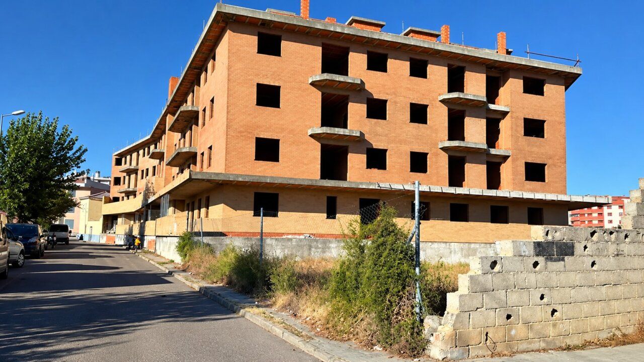 Edificio de vivienda inacabada en Zamora con ventanas vacías y vegetación alrededor.