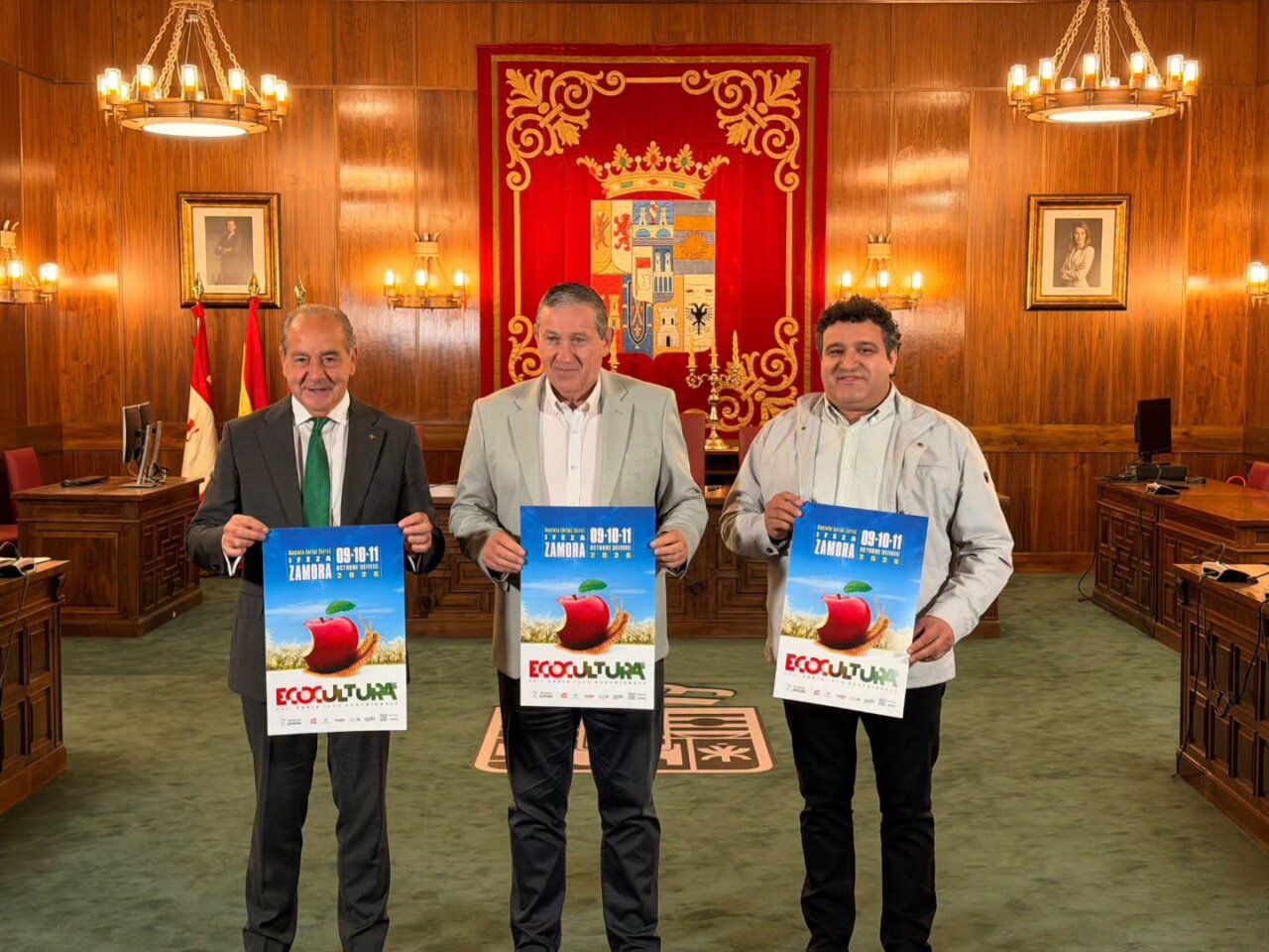 Tres hombres sosteniendo carteles de ECOCULTURA en un salón de actos