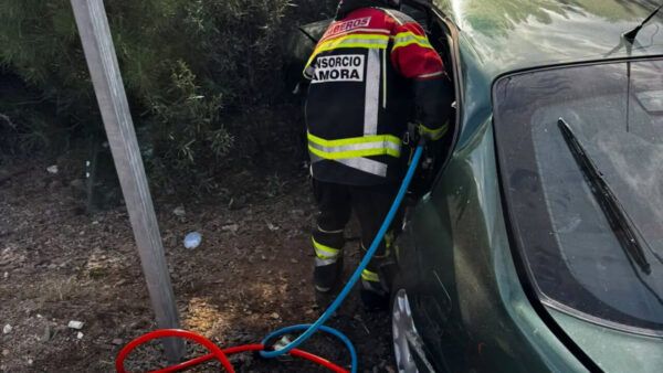 Un bombero junto a un coche, con mangueras tendidas en el suelo.