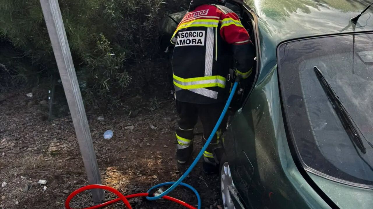 Un bombero junto a un coche, con mangueras tendidas en el suelo.