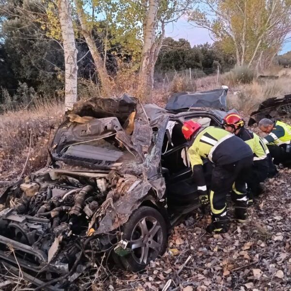 Bomberos trabajan junto a un coche muy dañado en una zona arbolada