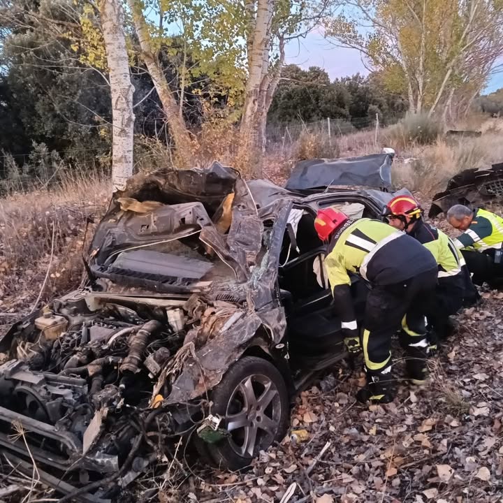 Bomberos trabajan junto a un coche muy dañado en una zona arbolada