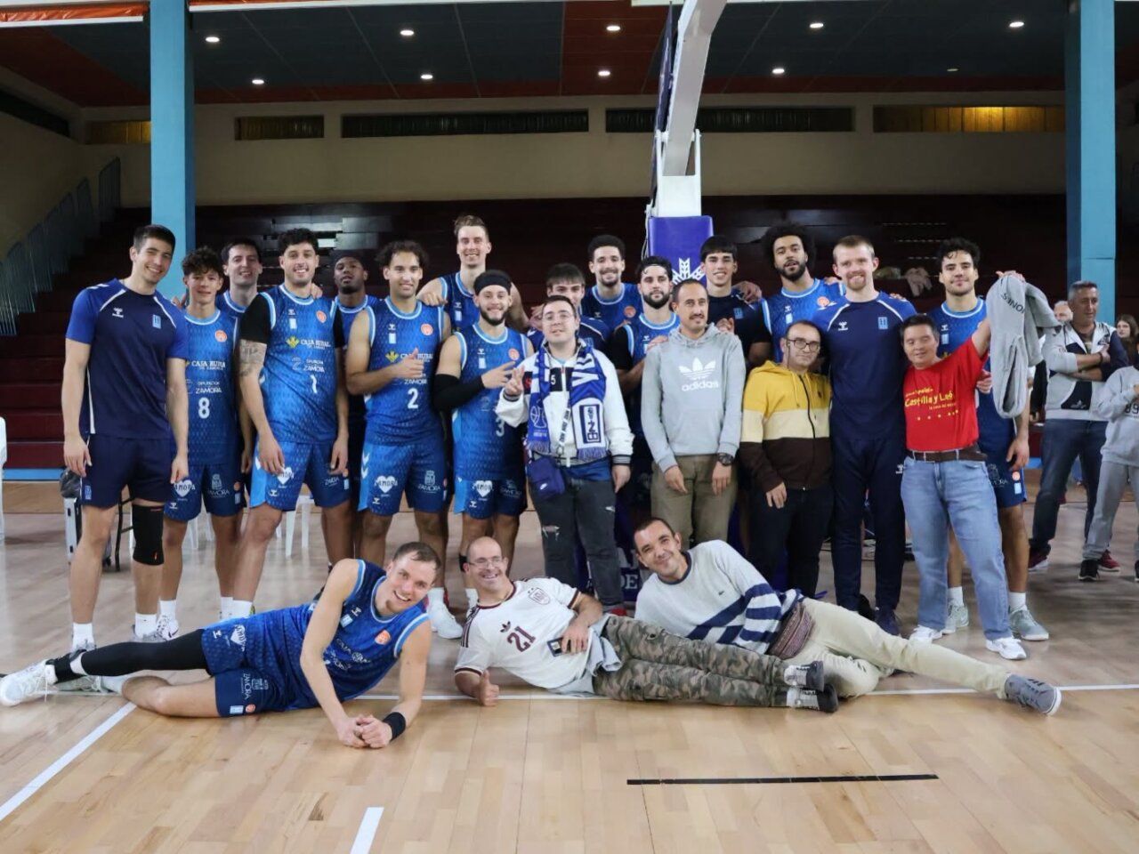 Jugadores de baloncesto con camisetas azules posan junto a varias personas en la pista
