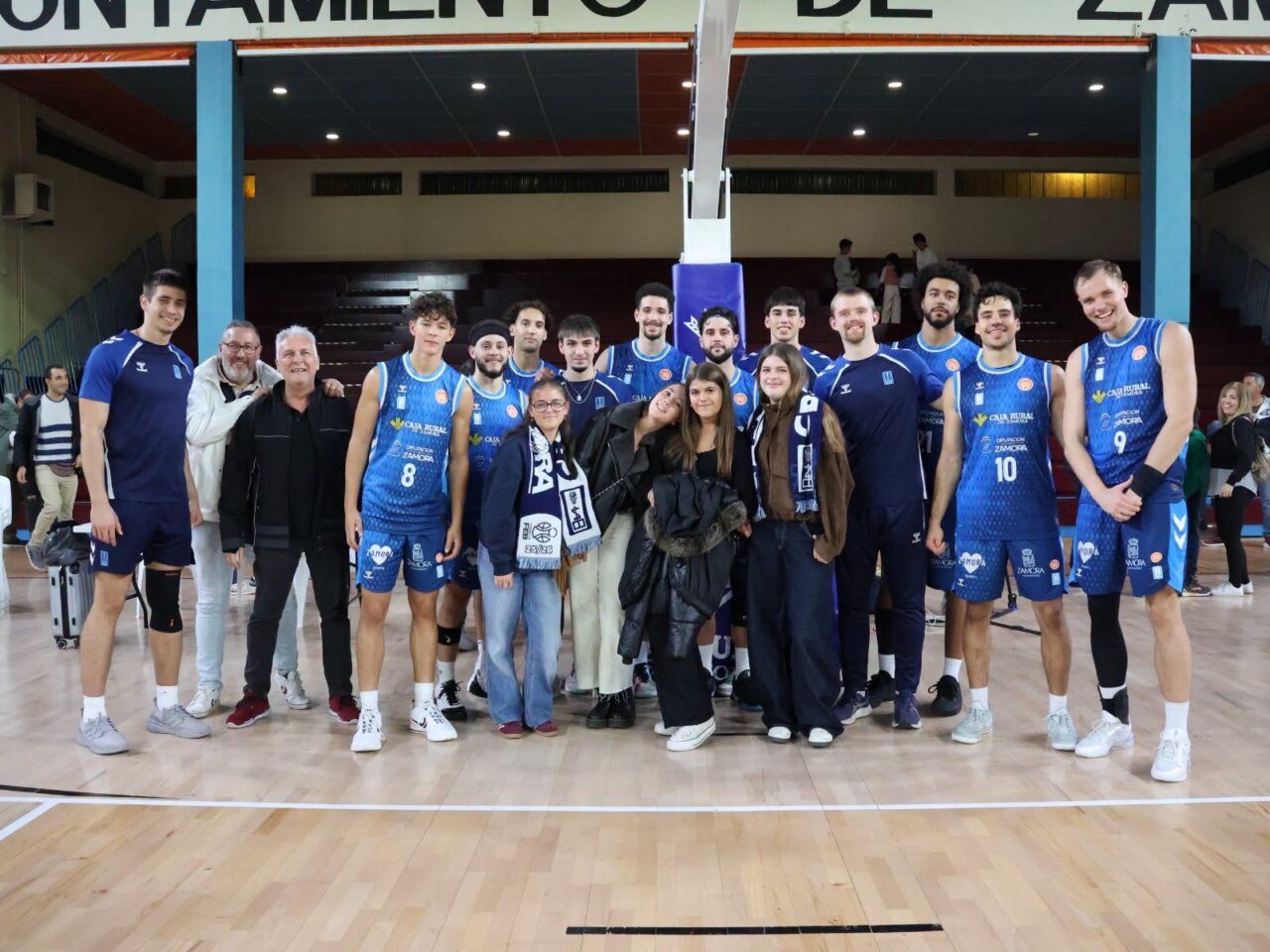 Jugadores del CB Zamora posan en una cancha de baloncesto con varias jóvenes y adultos.