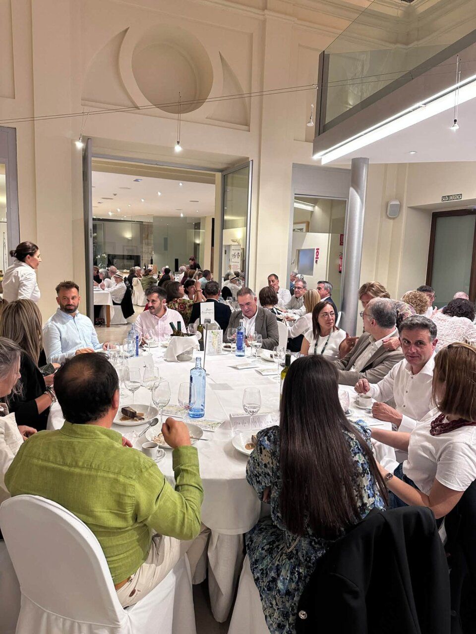 Asistentes sentados alrededor de mesas durante una cena en un salón amplio.