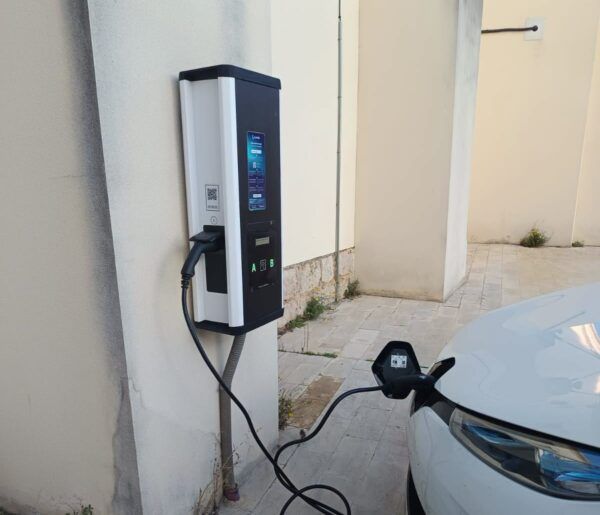 Un coche blanco conectado mediante cable a un punto de recarga junto a una pared.