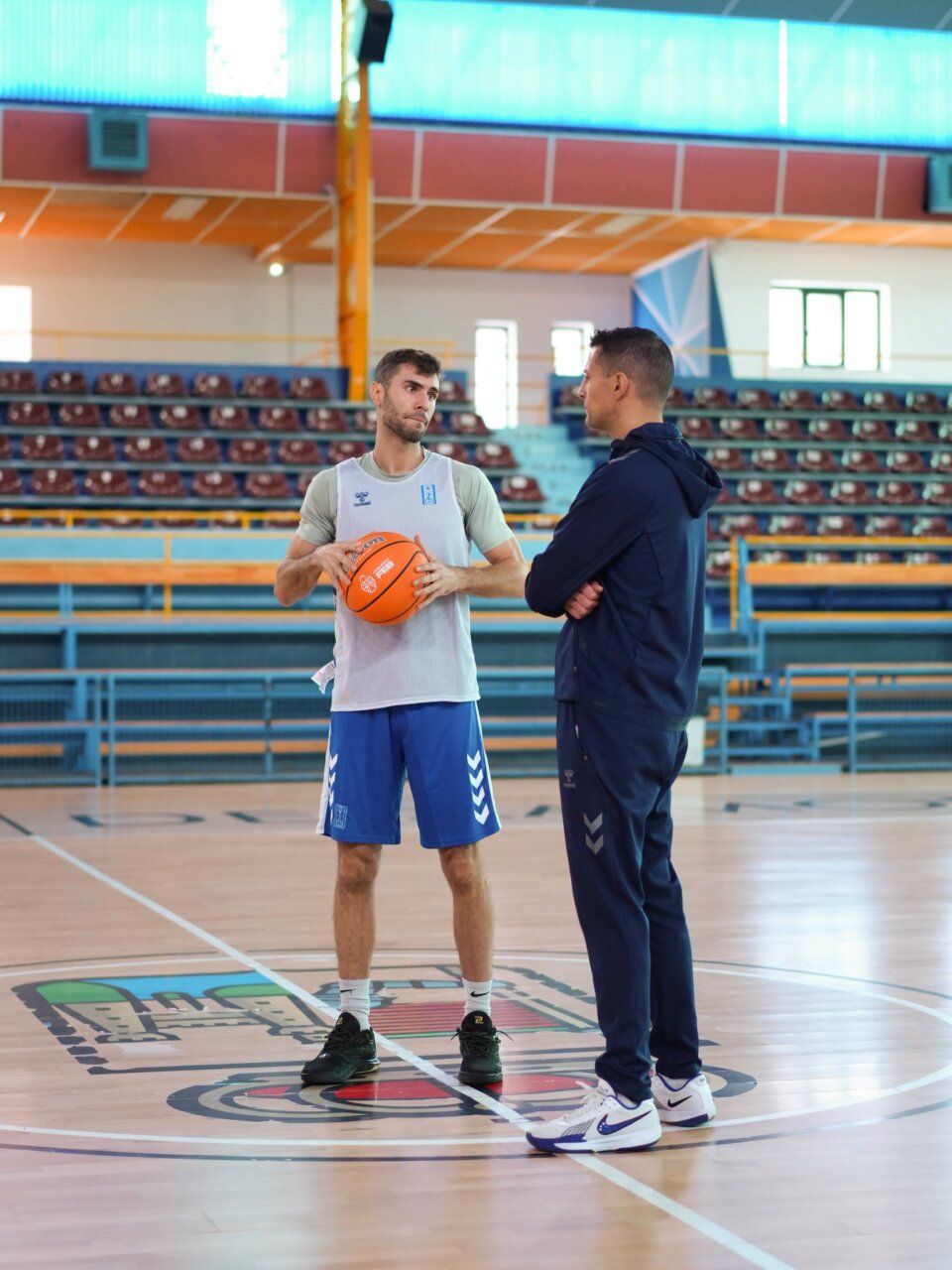 Dos hombres en una cancha de baloncesto; uno sostiene un balón naranja.