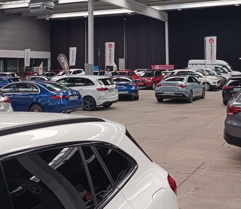 Varios automóviles expuestos en filas dentro de un amplio pabellón cubierto.