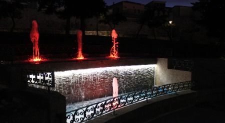 Fuente ornamental iluminada de noche, con chorros rojos y barandilla de hierro