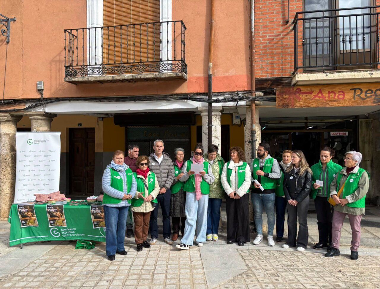 Grupo de personas con chalecos verdes junto a una mesa informativa en el exterior.