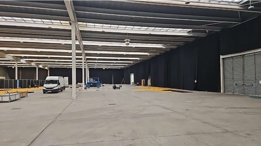 Interior amplio de un pabellón con suelo de hormigón, vehículos y estructura metálica.