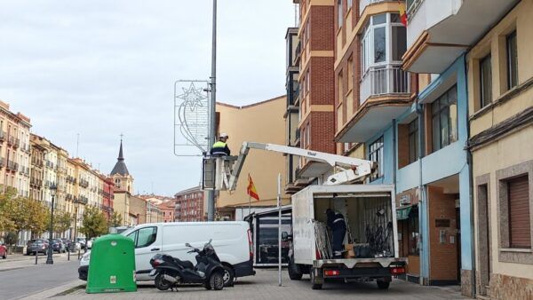 Operarios trabajan en un adorno luminoso navideño desde una plataforma junto a un camión.