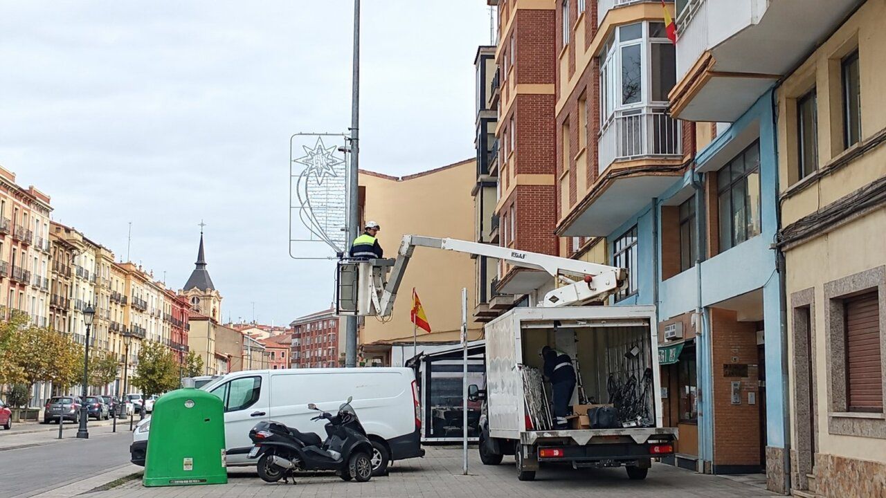 Operarios trabajan en un adorno luminoso navideño desde una plataforma junto a un camión.