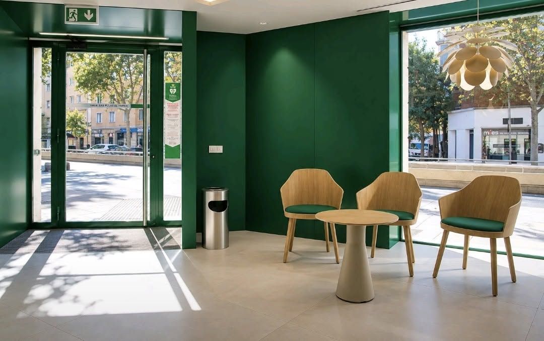 Interior luminoso con paredes verdes, tres sillones de madera y una mesa pequeña.
