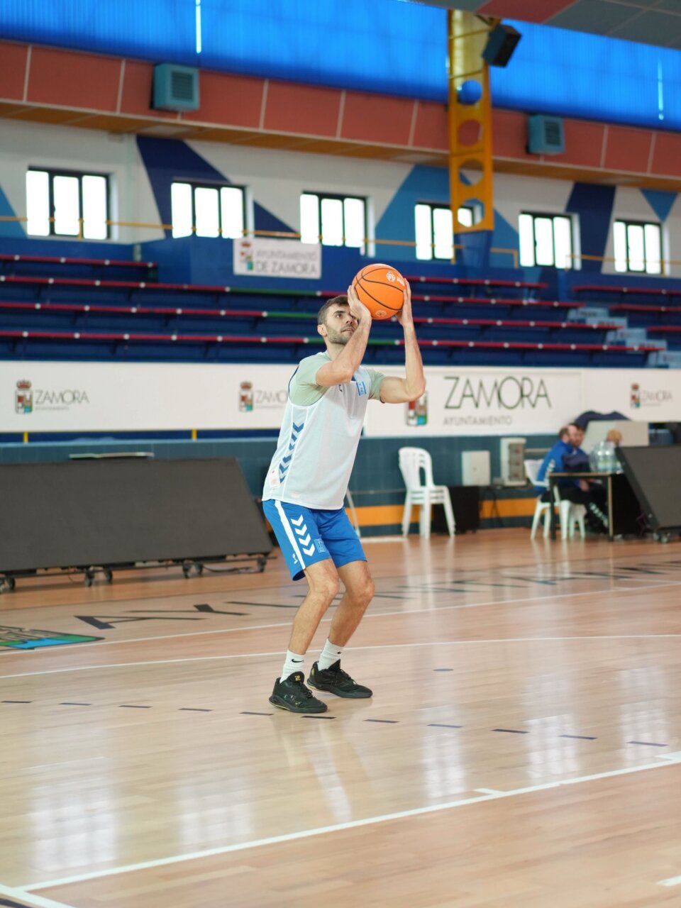 Jugador de baloncesto sostiene el balón en una pista cubierta antes de lanzar.