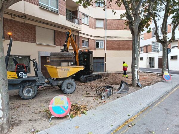 Maquinaria y un operario trabajan en un terreno junto a una acera arbolada