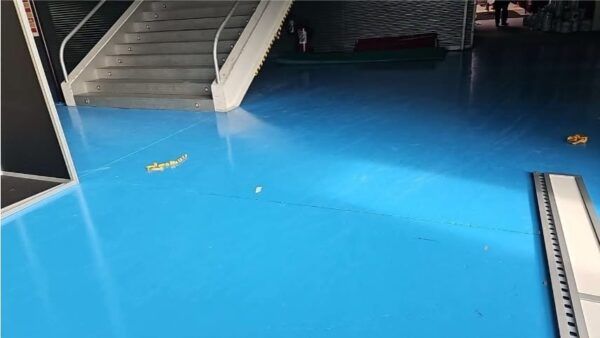 Pavimento azul de un pabellón junto a una escalera metálica y barandillas.