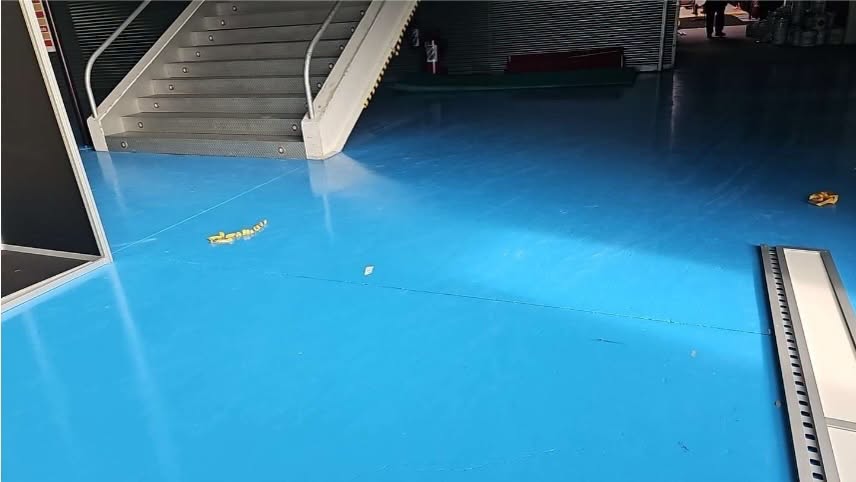 Pavimento azul de un pabellón junto a una escalera metálica y barandillas.