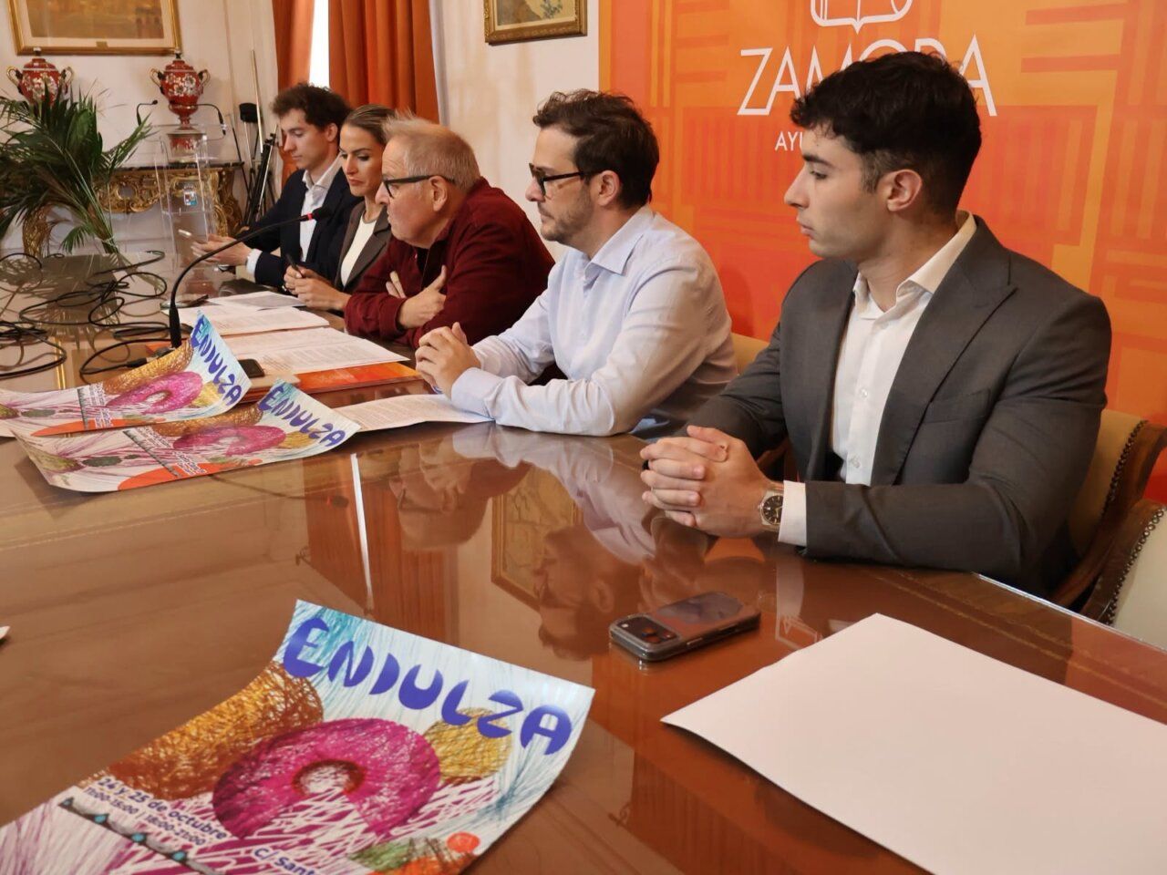 Varias personas sentadas ante una mesa con folletos de ENDULZA y fondo naranja.