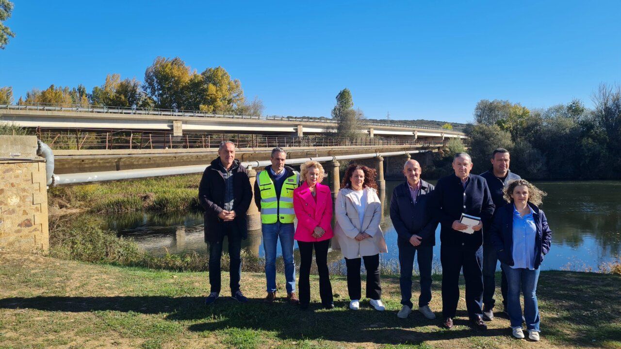 Grupo de personas posa junto a un puente sobre un río, con otro puente detrás