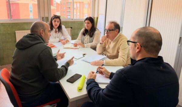 Cinco personas conversan alrededor de una mesa con cuadernos y bolígrafos.