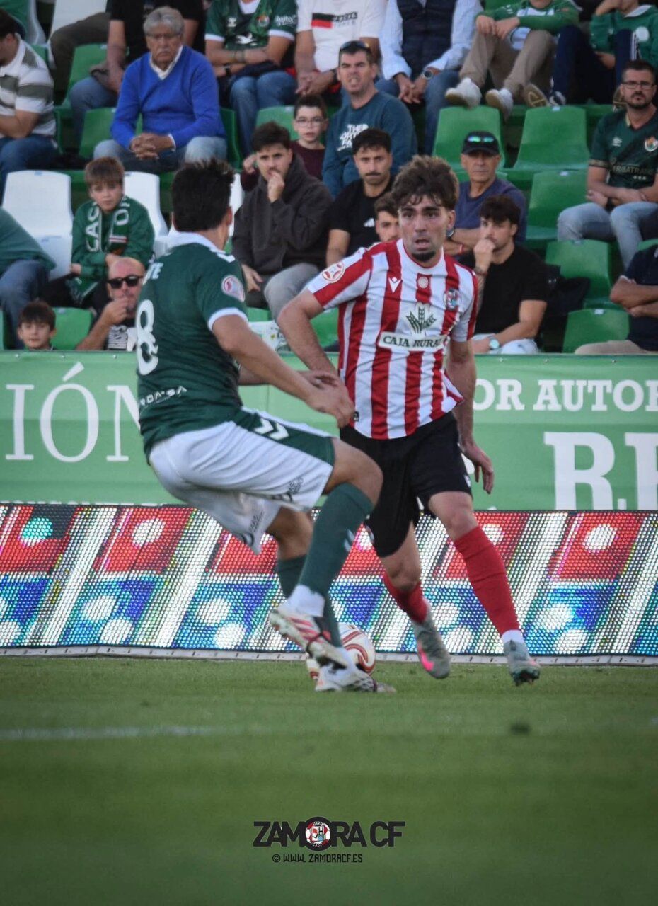 Un jugador del Zamora CF disputa el balón ante un rival vestido de verde.