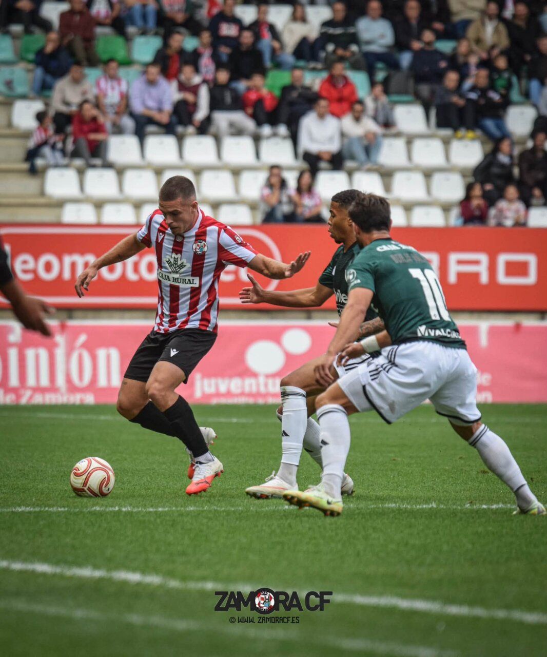 Futbolista rojiblanco conduce el balón ante jugadores de verde en un partido.