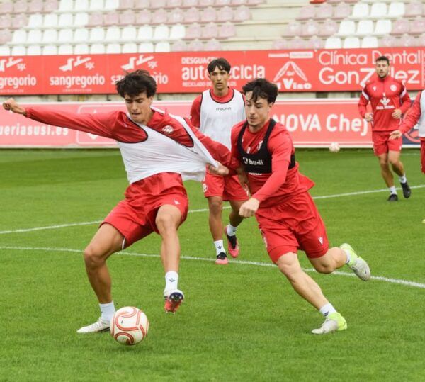 Futbolistas con equipación roja disputan el balón durante un entrenamiento sobre el césped.