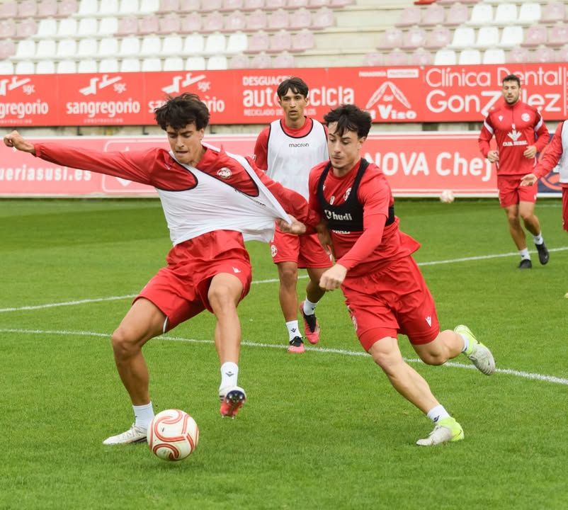 Futbolistas con equipación roja disputan el balón durante un entrenamiento sobre el césped.